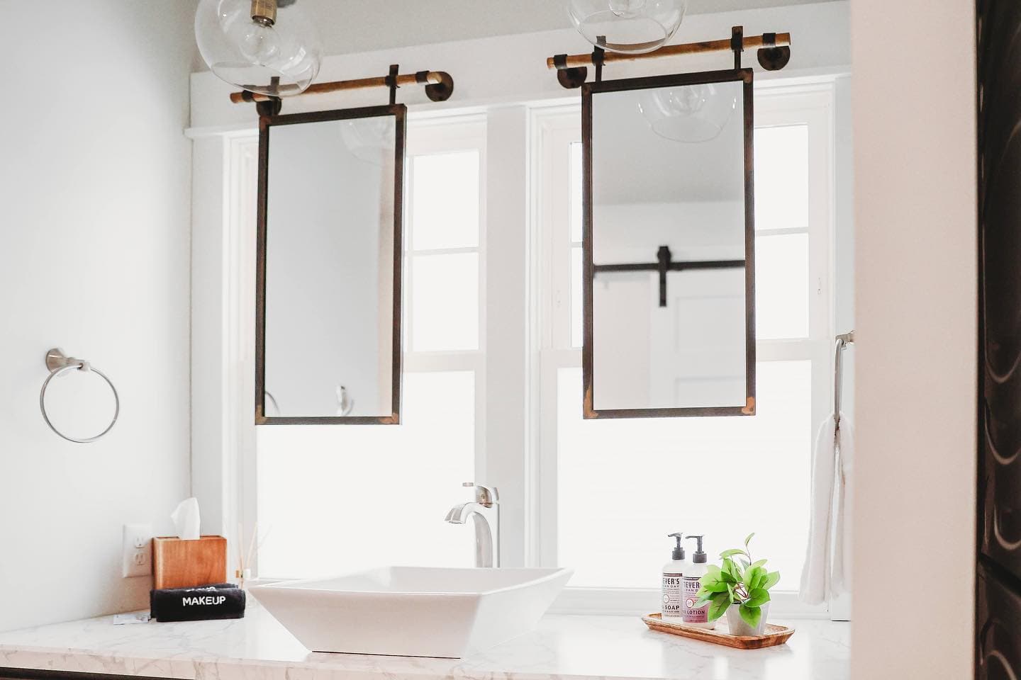 Two mirrors on sliding tracks hang over a white vessel sink and marble countertop.