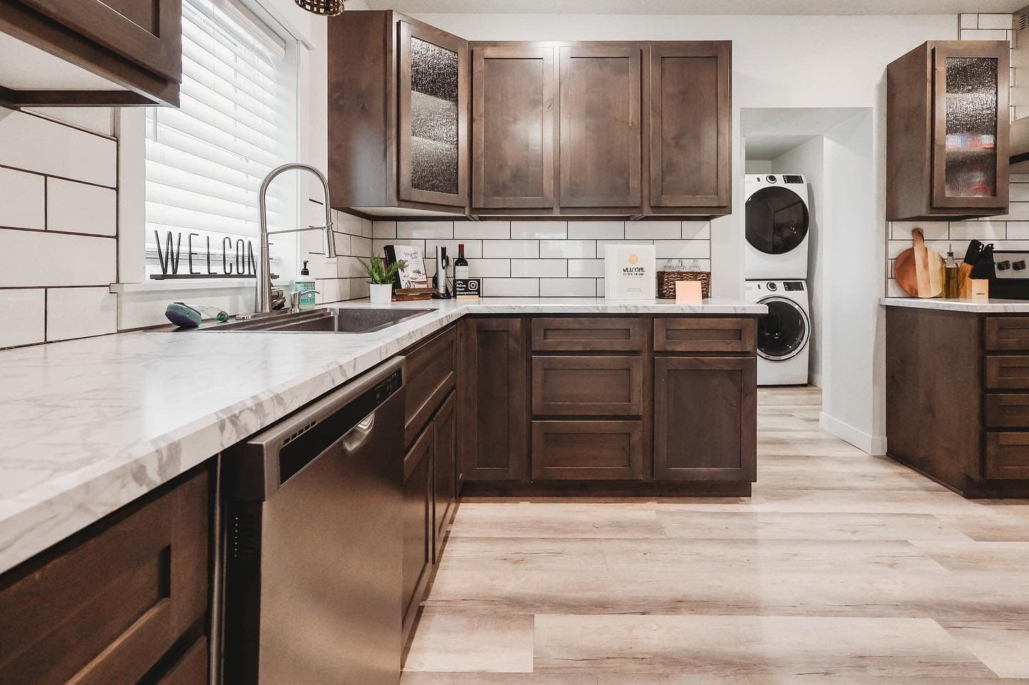 Modern kitchen featuring dark wood cabinets, marble countertops, and a stacked washer and dryer.