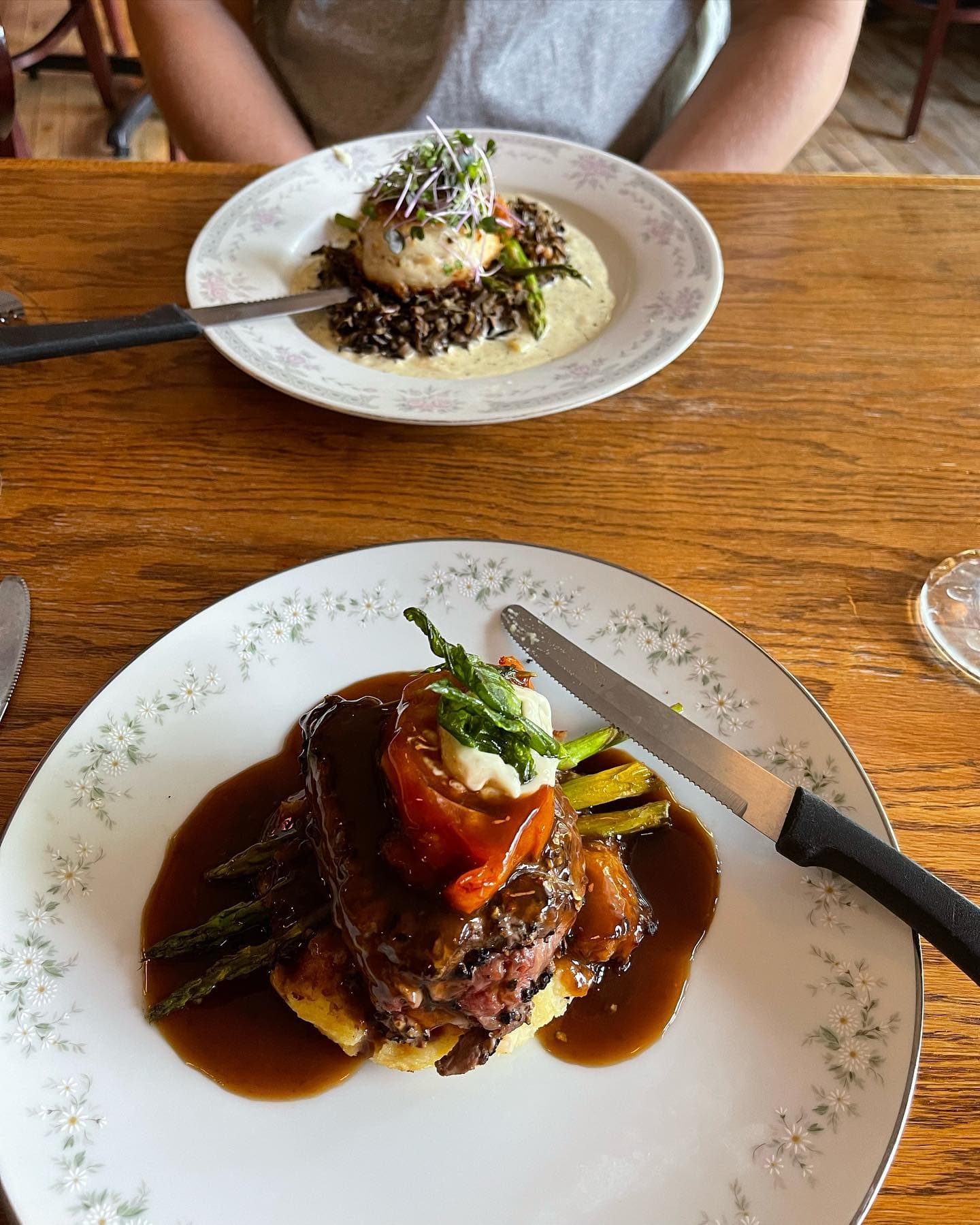 Steak with asparagus and gravy on a floral plate, with another dish in the background.