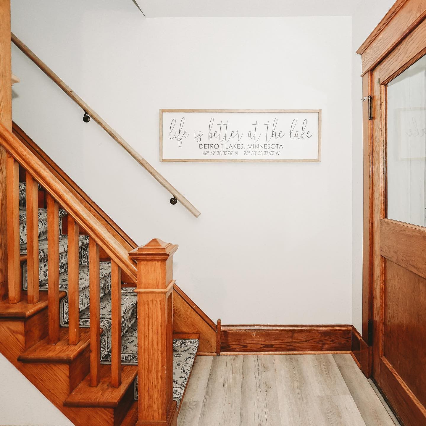 Wooden staircase with patterned runner and a sign reading life is better at the lake.