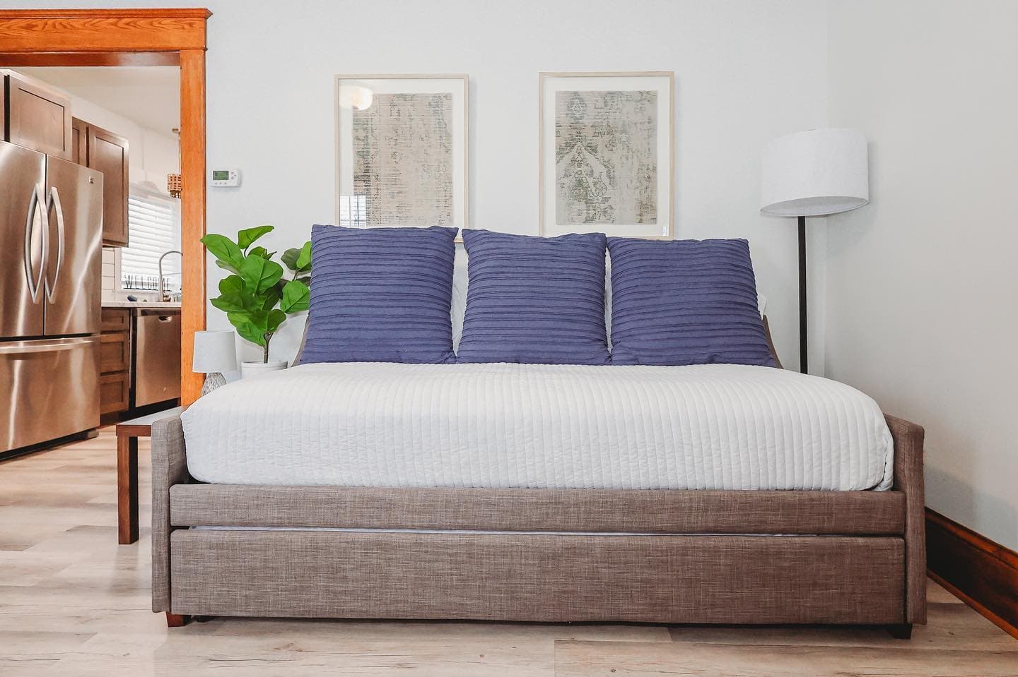 Modern daybed with white bedding and three purple pillows, positioned near a kitchen doorway.