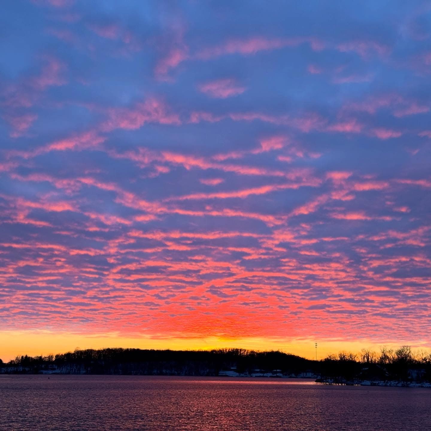 Vibrant pink and orange clouds reflect over a calm lake during a dramatic sunset.