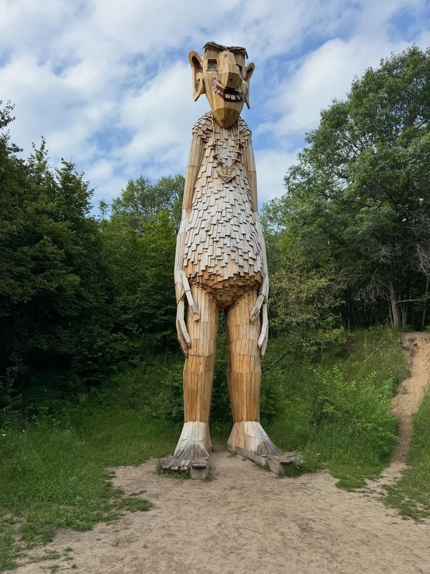Towering wooden troll sculpture with a shingled body standing in a lush green forest clearing.
