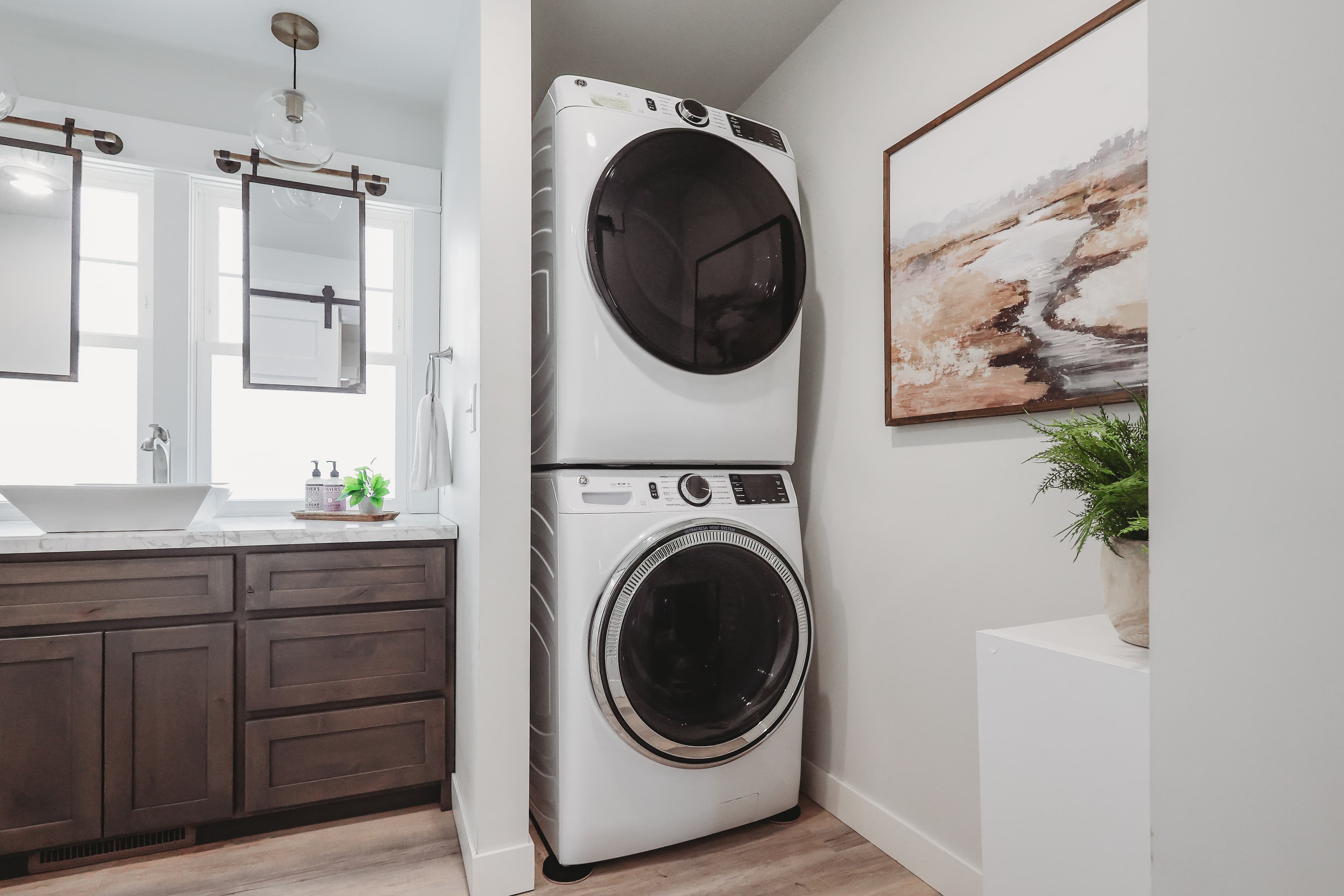 Stacked white washer and dryer unit next to a dark wood vanity with vessel sink.