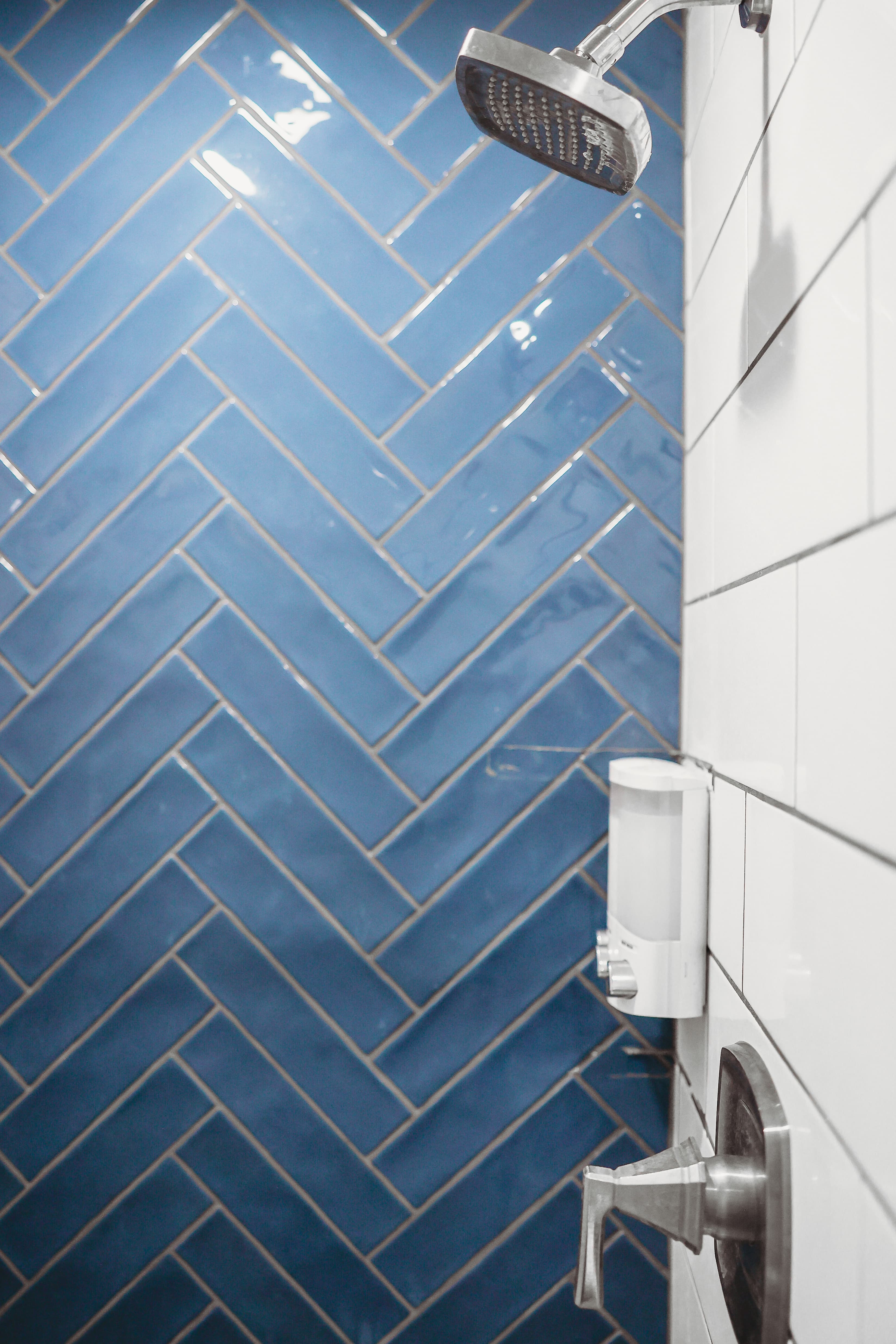 Modern shower with blue herringbone tiles, chrome showerhead, and white subway tile wall.