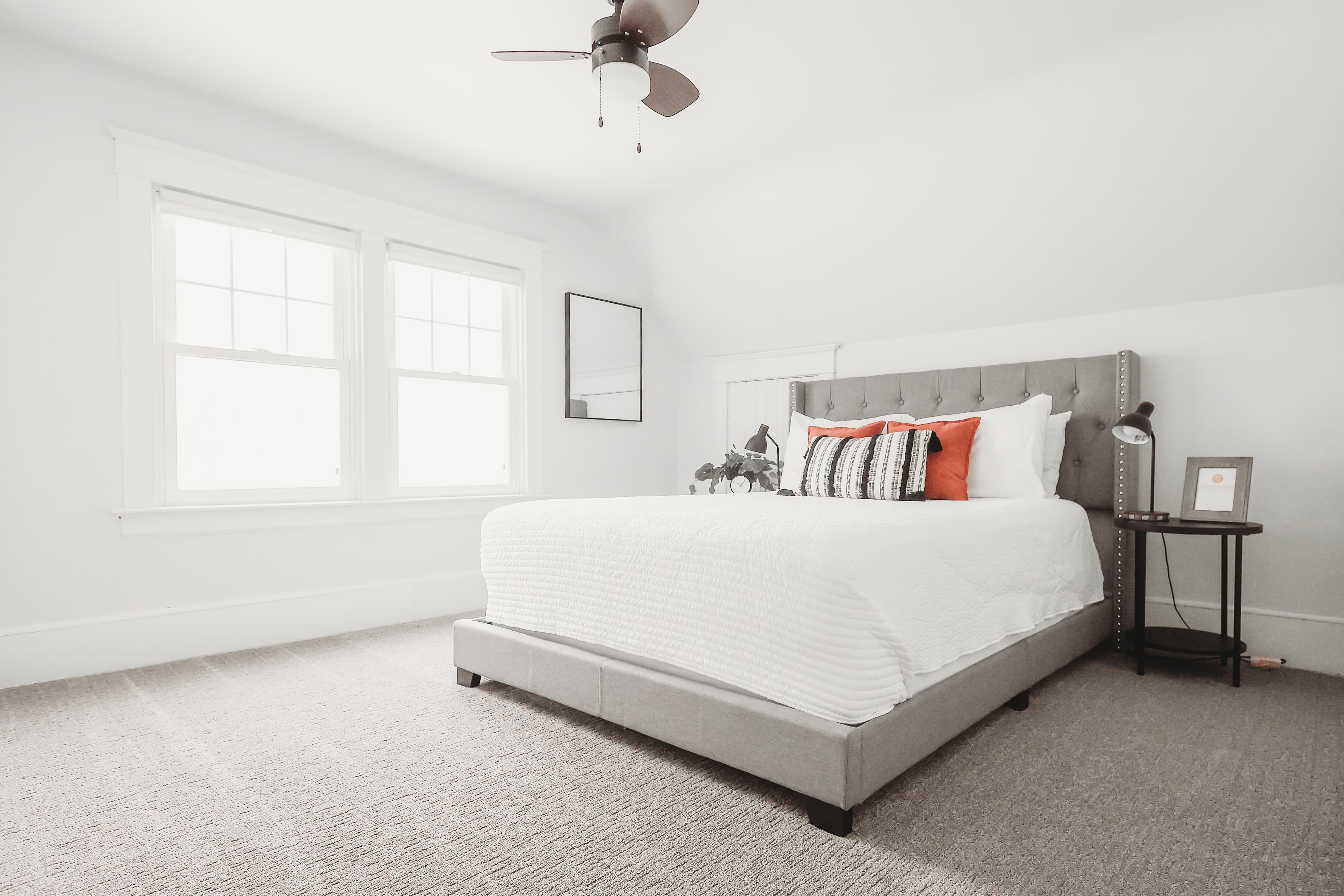 Bright bedroom featuring a grey tufted bed with white bedding and orange accent pillows.