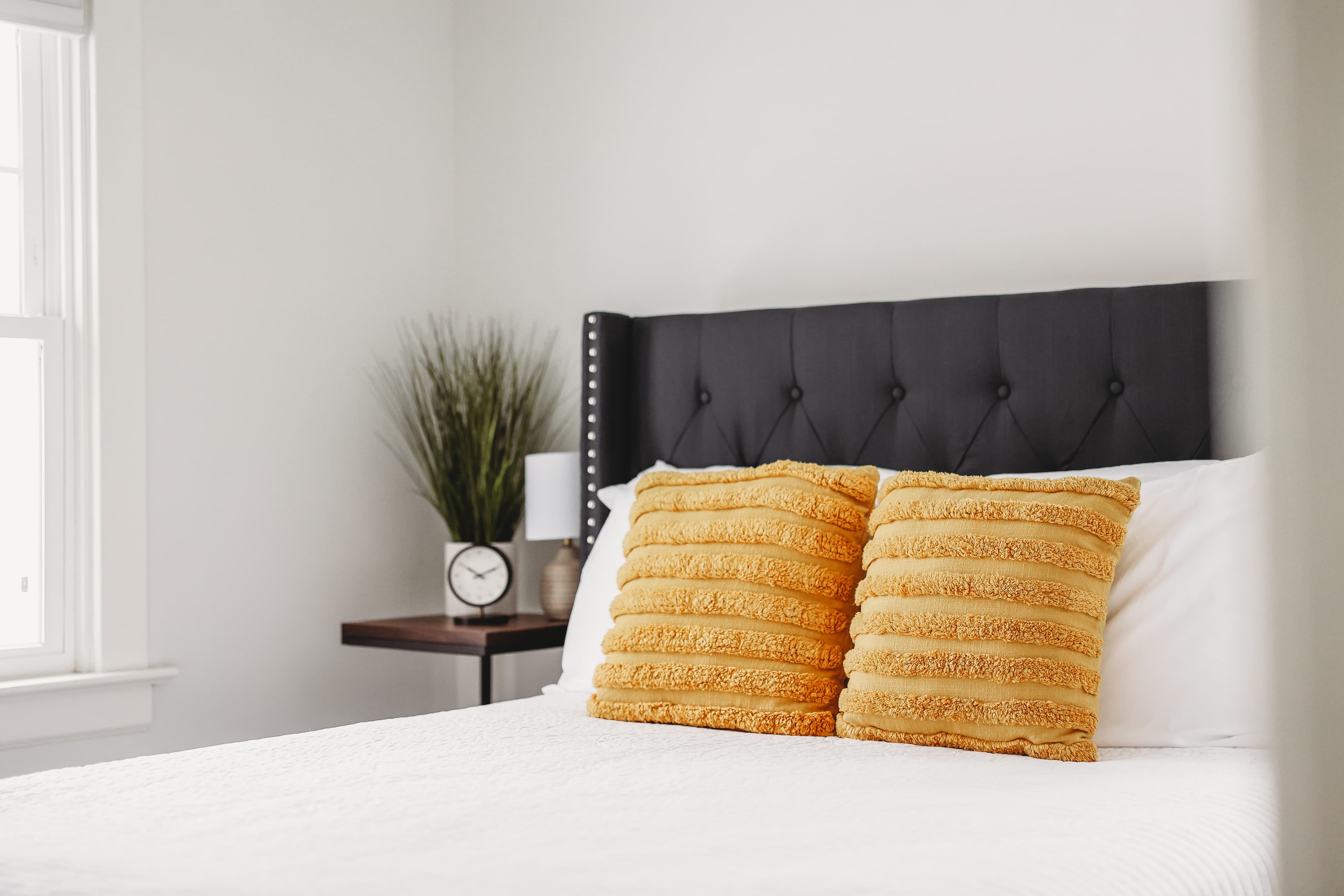 Bed with a dark grey tufted headboard, white bedding, and two yellow textured throw pillows.