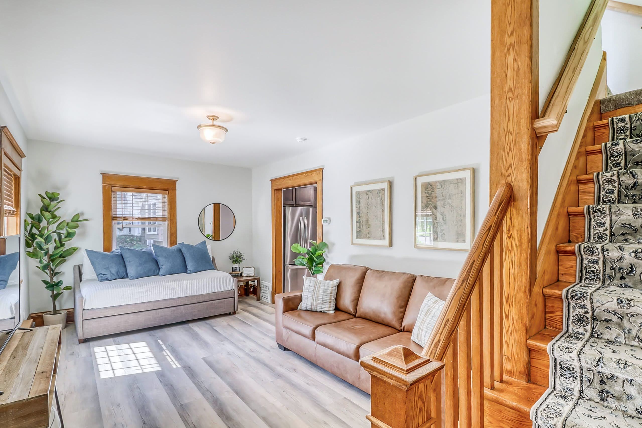 Bright living room with brown leather sofa, daybed, and wooden stairs with patterned runner.