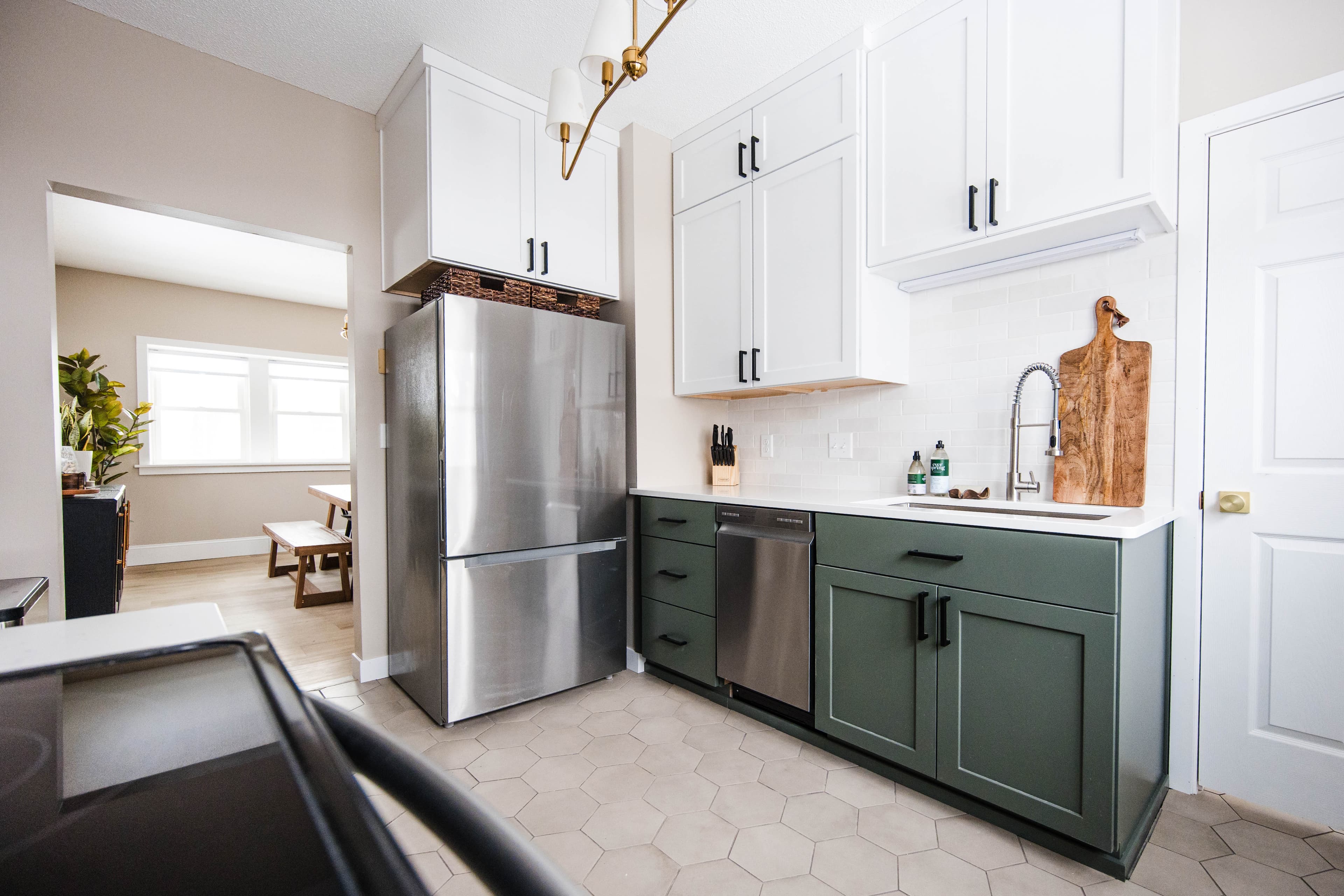 Modern kitchen with white upper and green lower cabinets, stainless steel appliances, and hexagonal tiles.