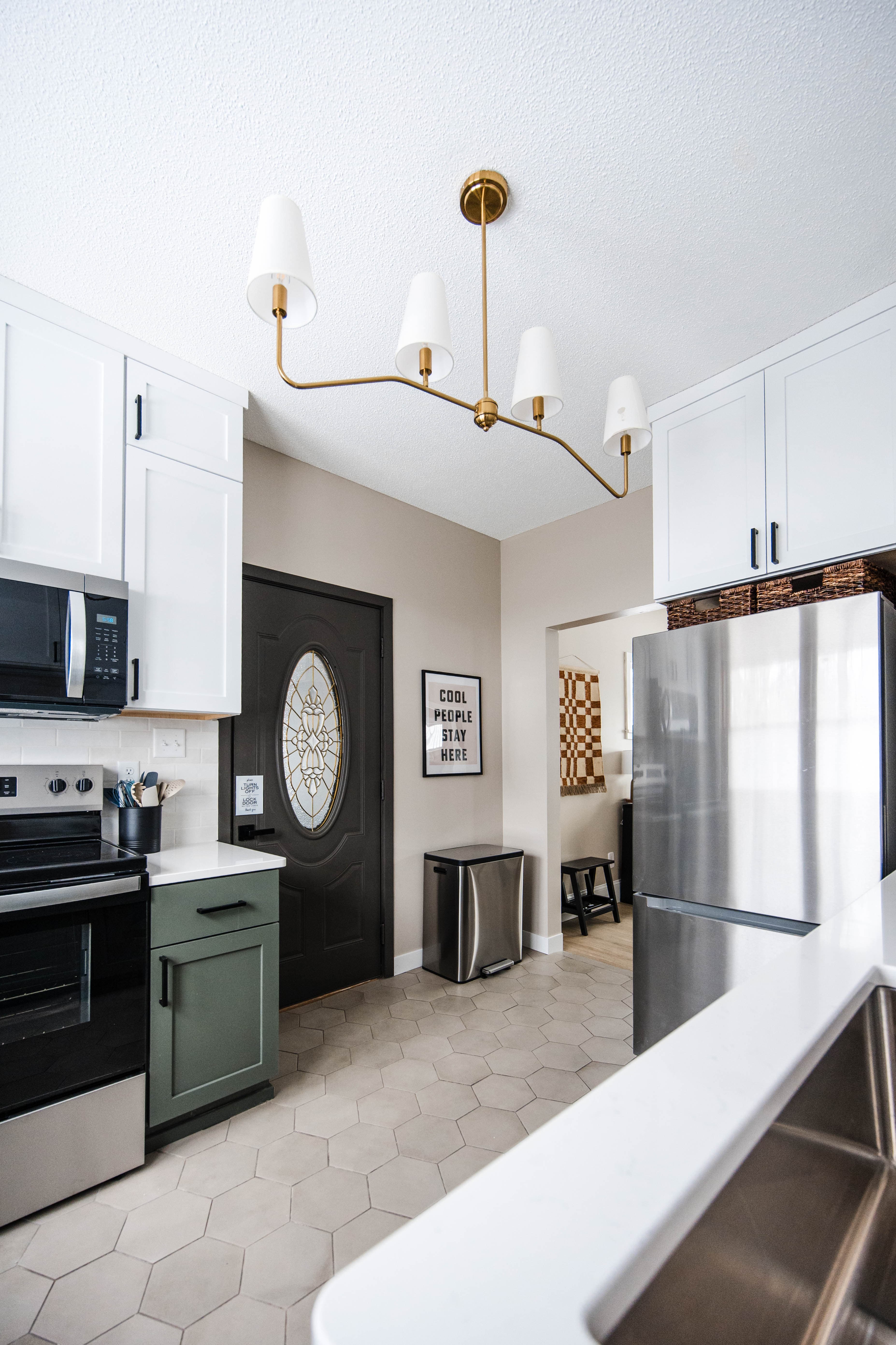 Modern kitchen with white and green cabinets, stainless steel appliances, and a gold chandelier.