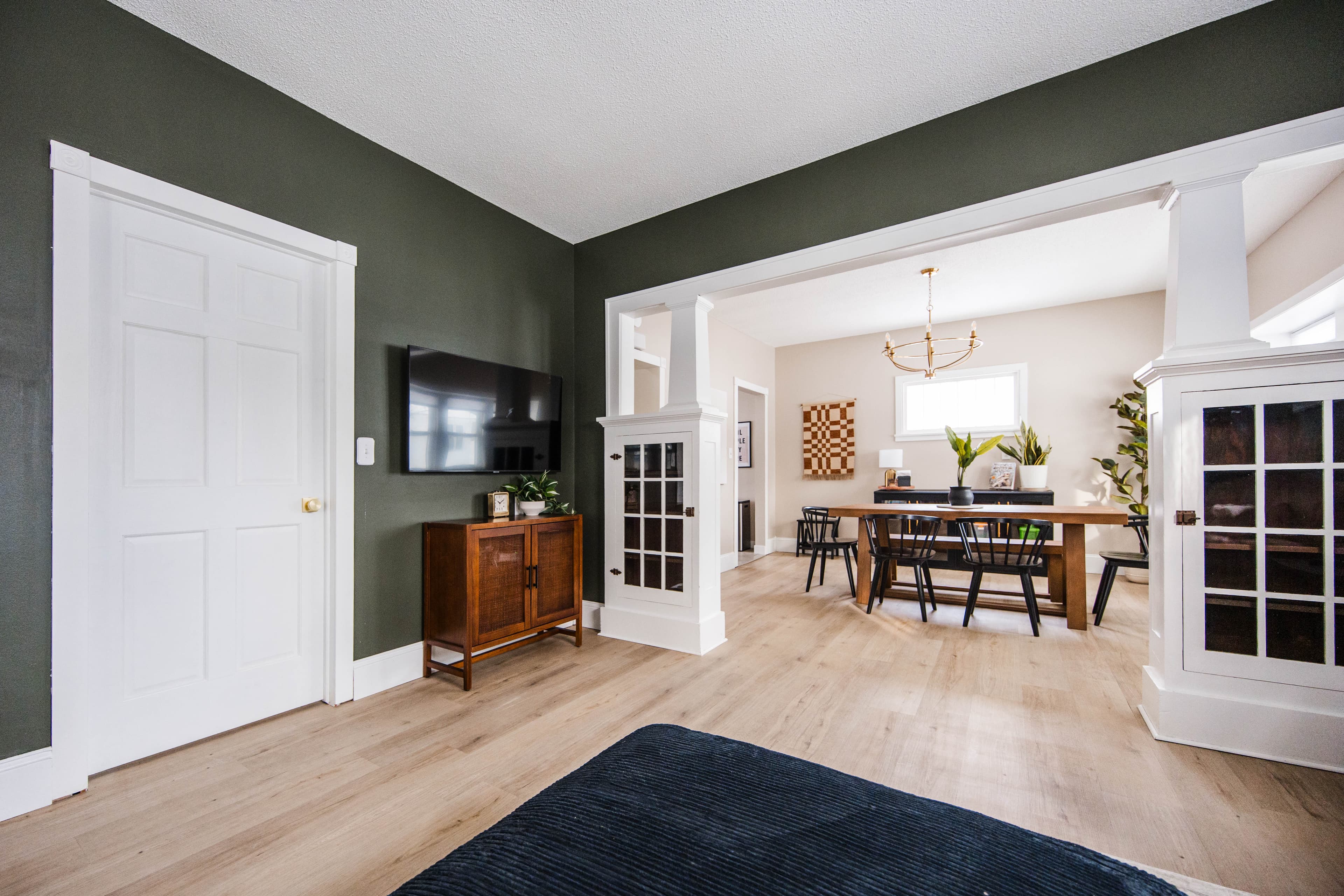 Dark green living room with a TV, opening into a bright, modern dining space.