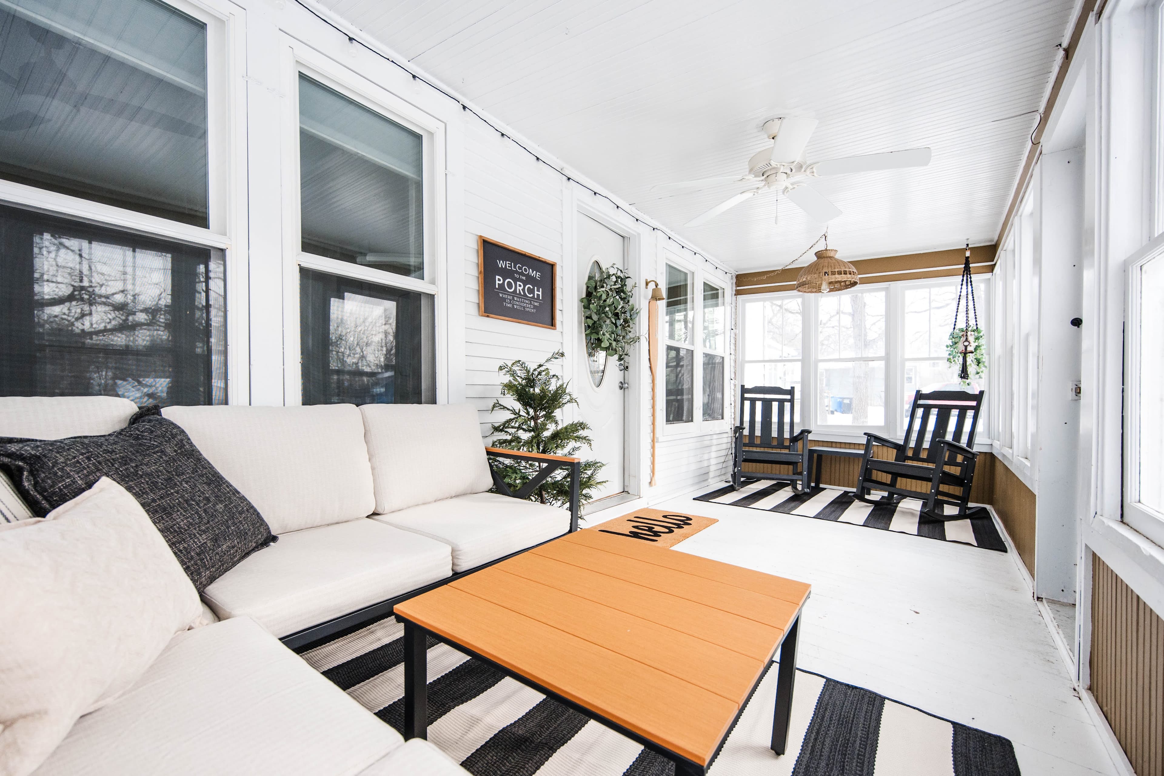 Bright white sunroom with a white sectional, wooden coffee table, and black rocking chairs.
