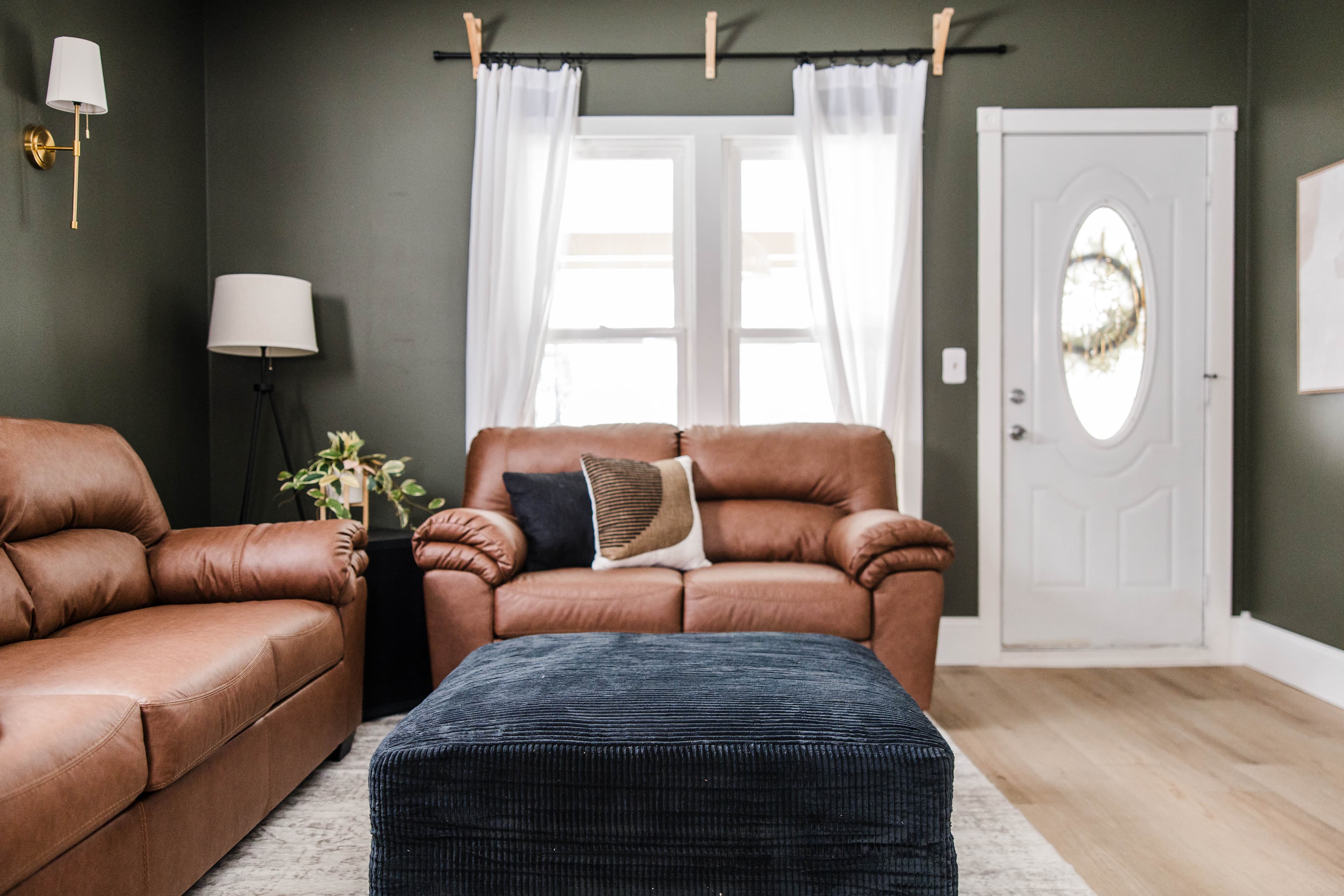 Cozy living room with dark green walls, brown leather sofas, and a blue corduroy ottoman.