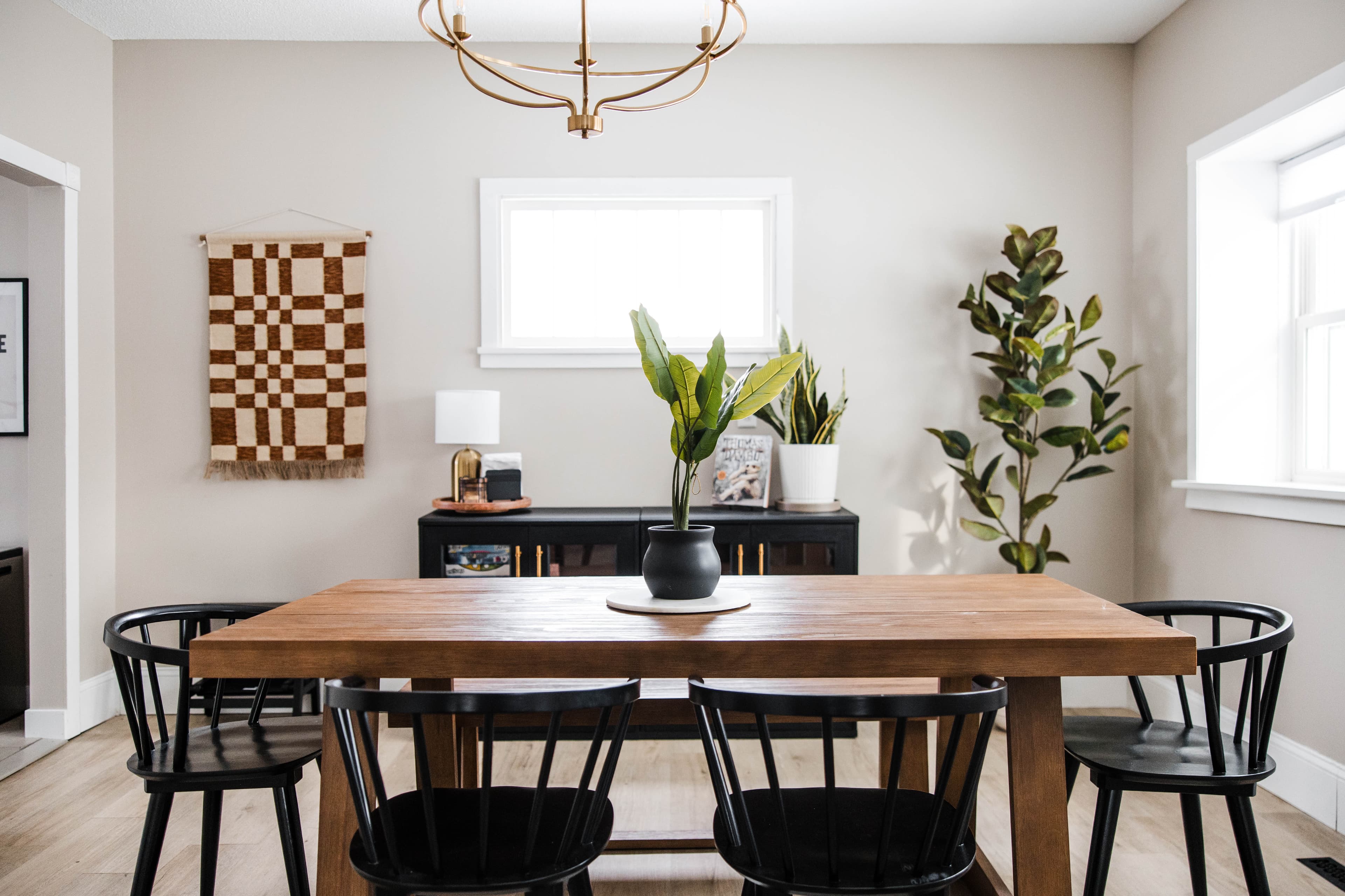Modern dining room featuring a wooden table, black spindle chairs, and minimalist decor with plants.