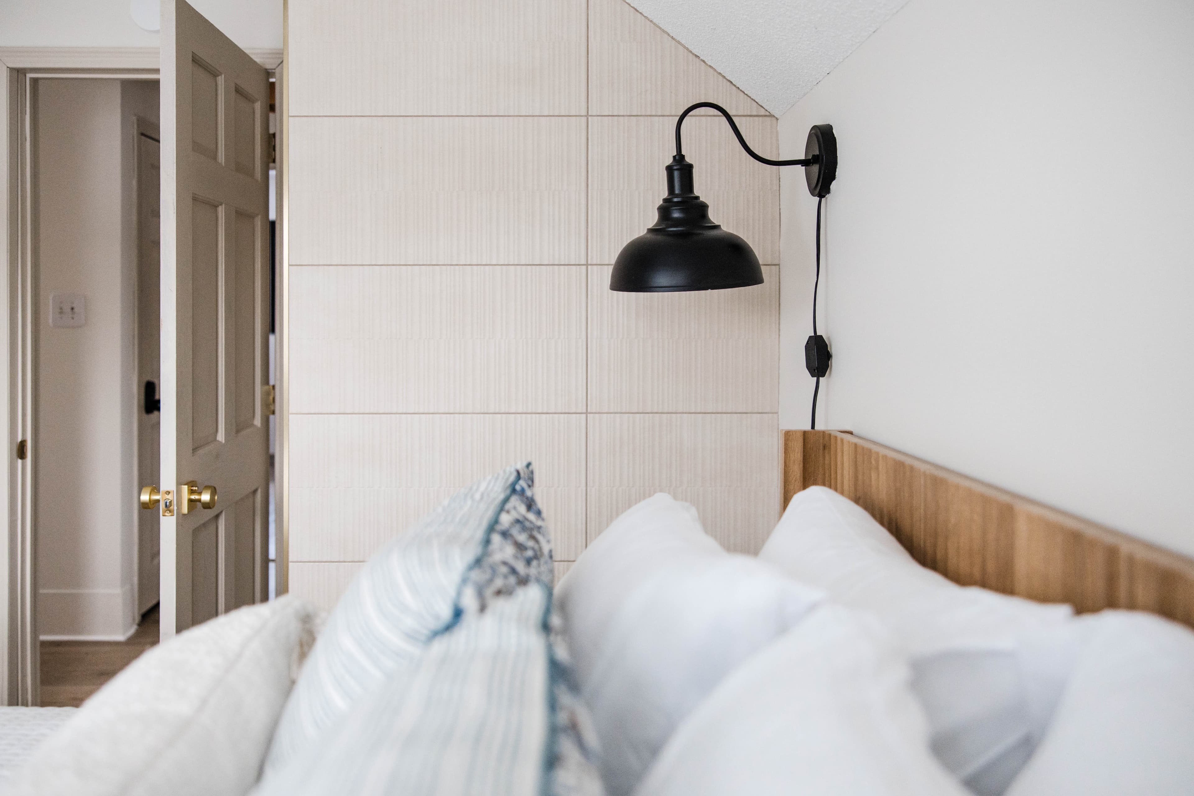 Black wall sconce mounted above a wooden headboard with plush white and blue pillows.