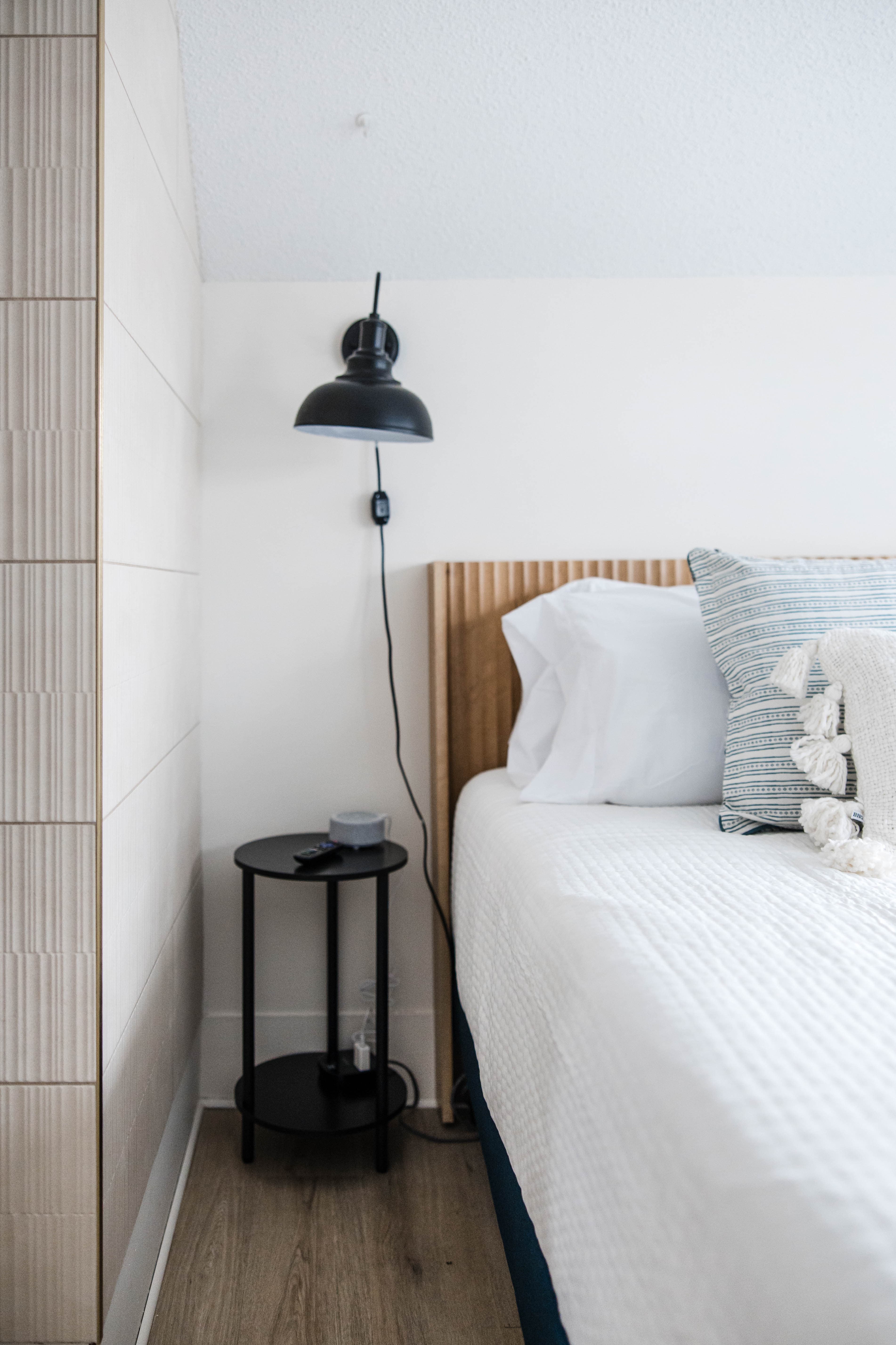 Modern bedroom corner with black wall lamp, small side table, and bed with white linens.