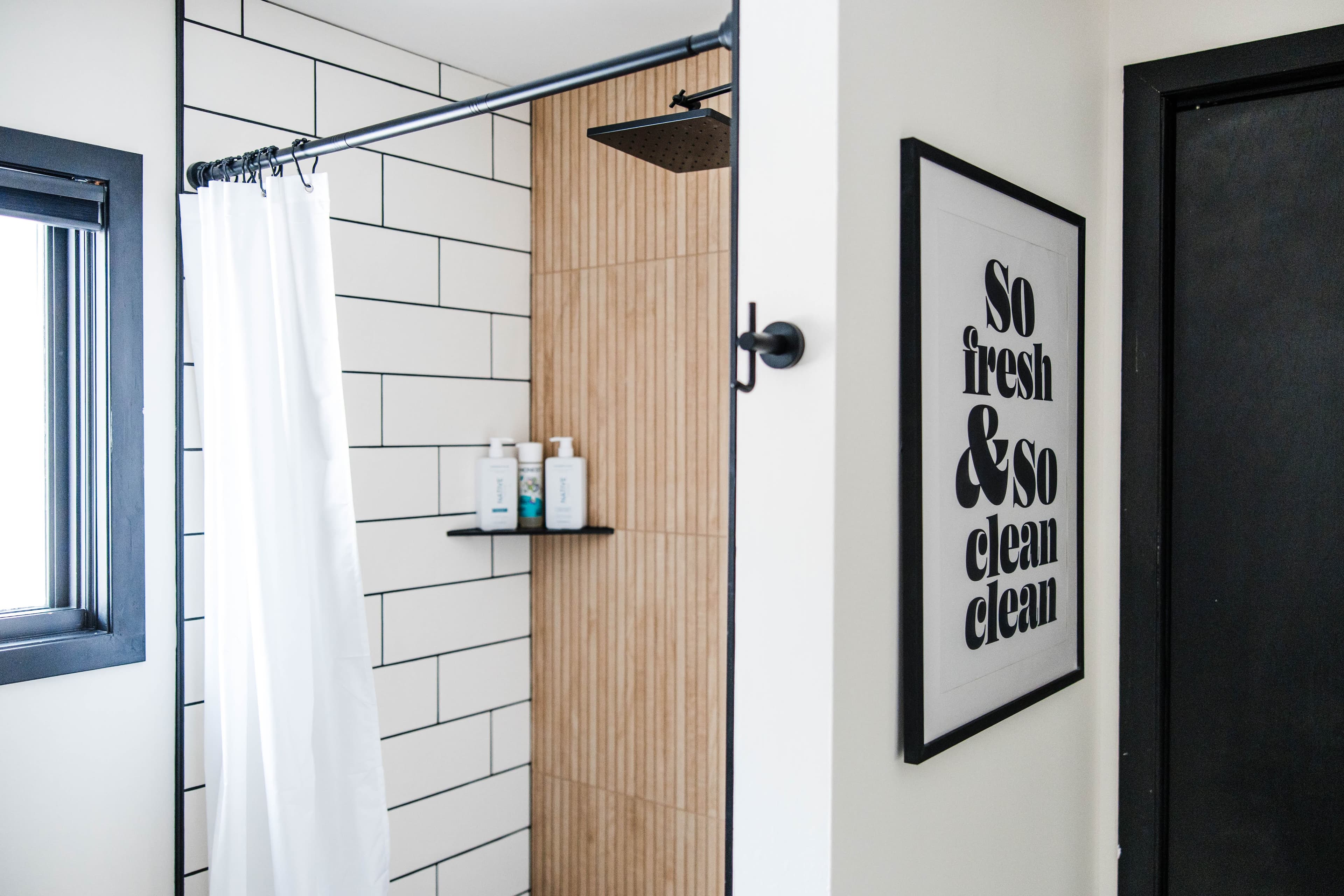 Modern bathroom with subway tiles, wood-slat wall, and "So fresh & so clean clean" print.